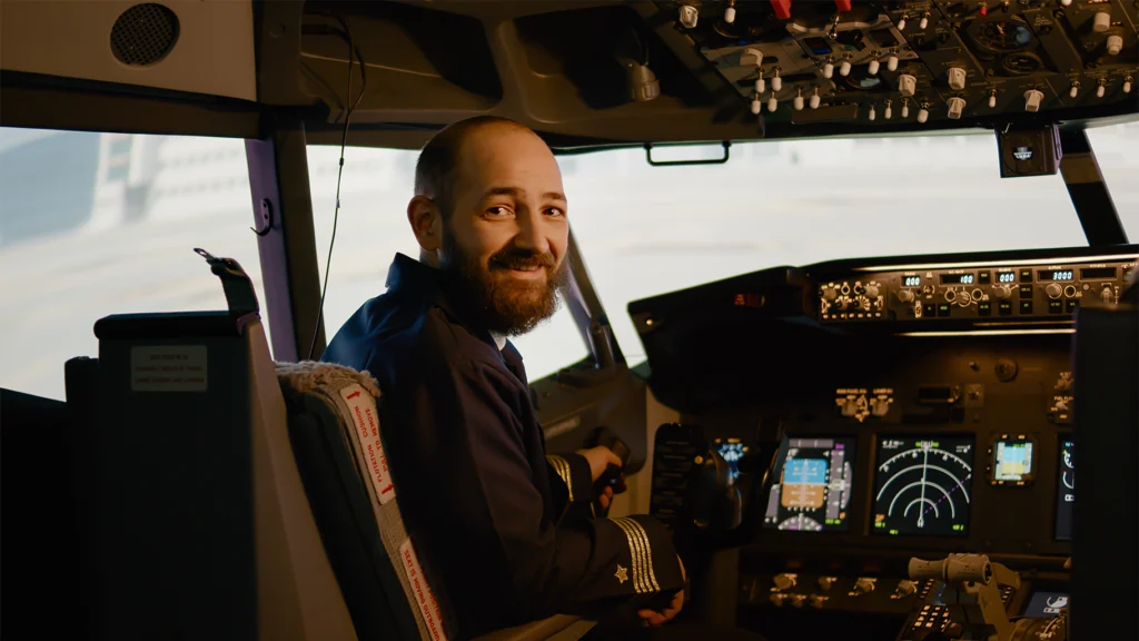 Veteran Air Warriors pilot sitting in airplane cockpit turns around to smile at camera.